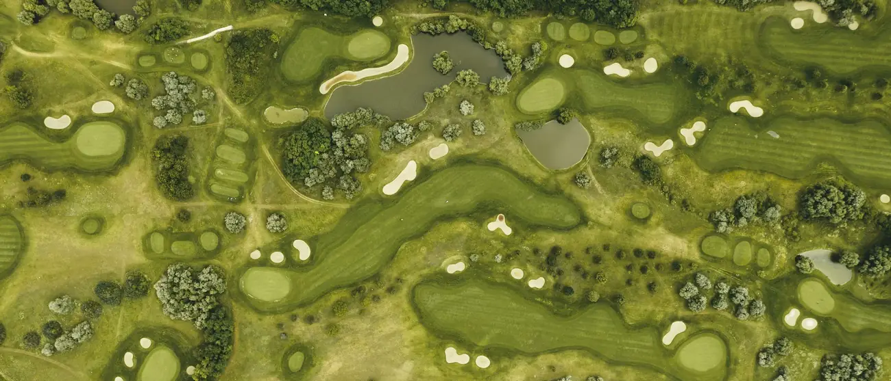 Vista aérea cenital de un recorrido de golf con greens, búnkeres, lagos y arbolado
